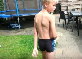 Boy Blond hair in swimsuit blue playing with "roller board" in the streets